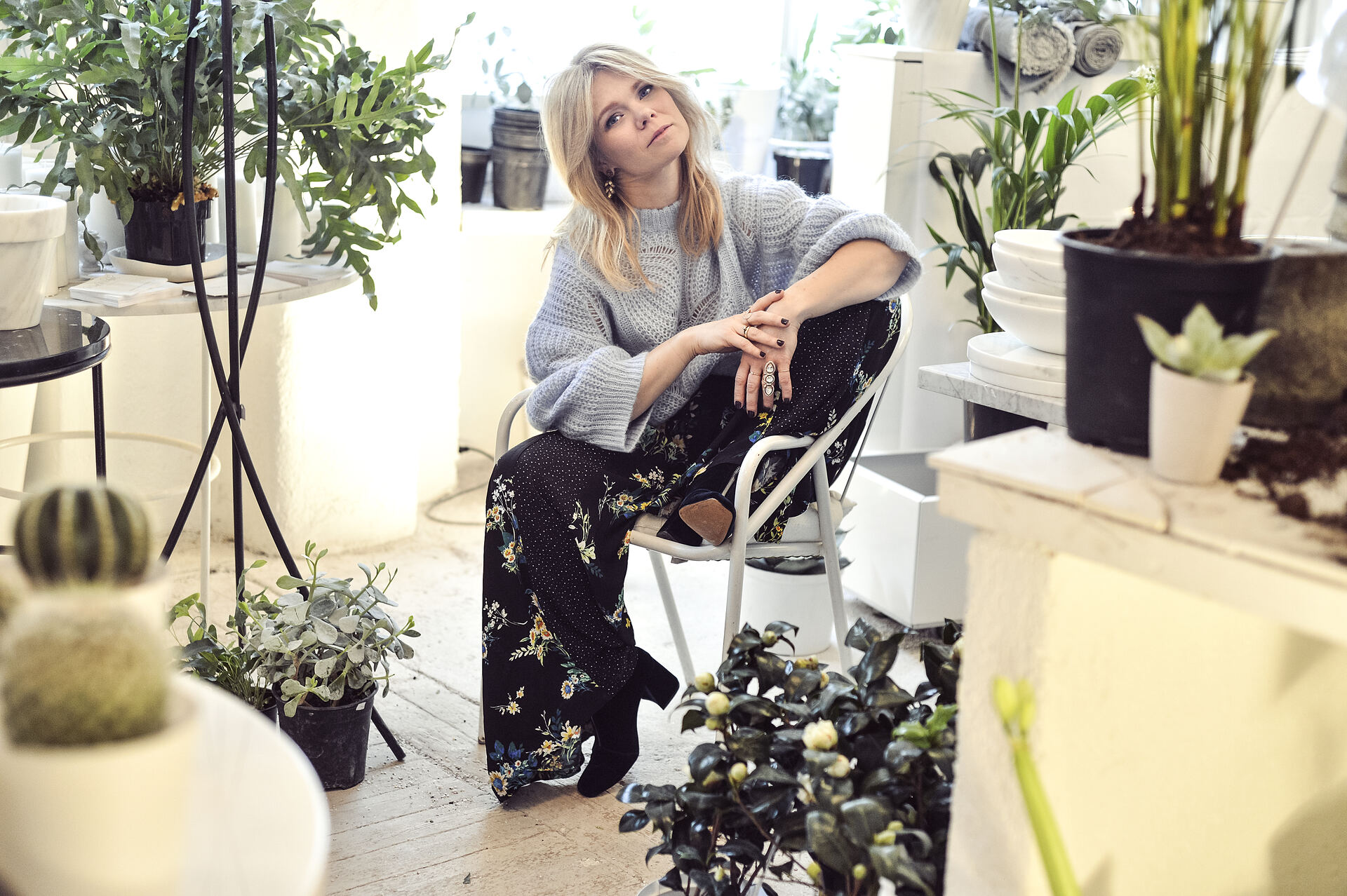 Kristin Minde sitter på en stol blant grønne planter i et lyst rom